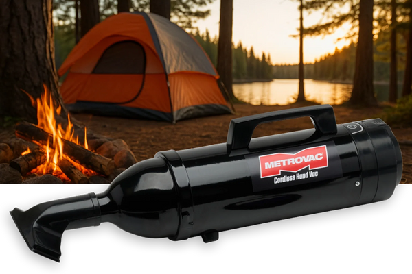 Metrovac Cordless Hand Vac placed at a campsite near a campfire and orange tent by a lake at sunset.