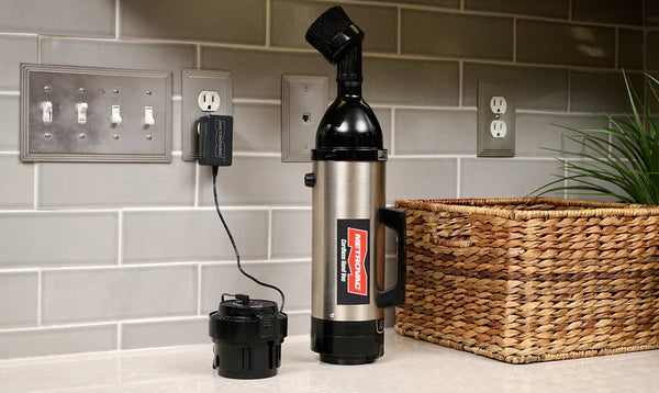 MetroVac cordless vacuum charging on a kitchen countertop with dual battery pack and fast-charger plugged into wall.