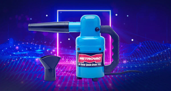 MetroVac Air Force® Quick Draw® Mini handheld dryer displayed in bright blue with black nozzle attachment, set against a neon gaming-style background featuring pink and blue glowing grid lines and a futuristic light frame.
