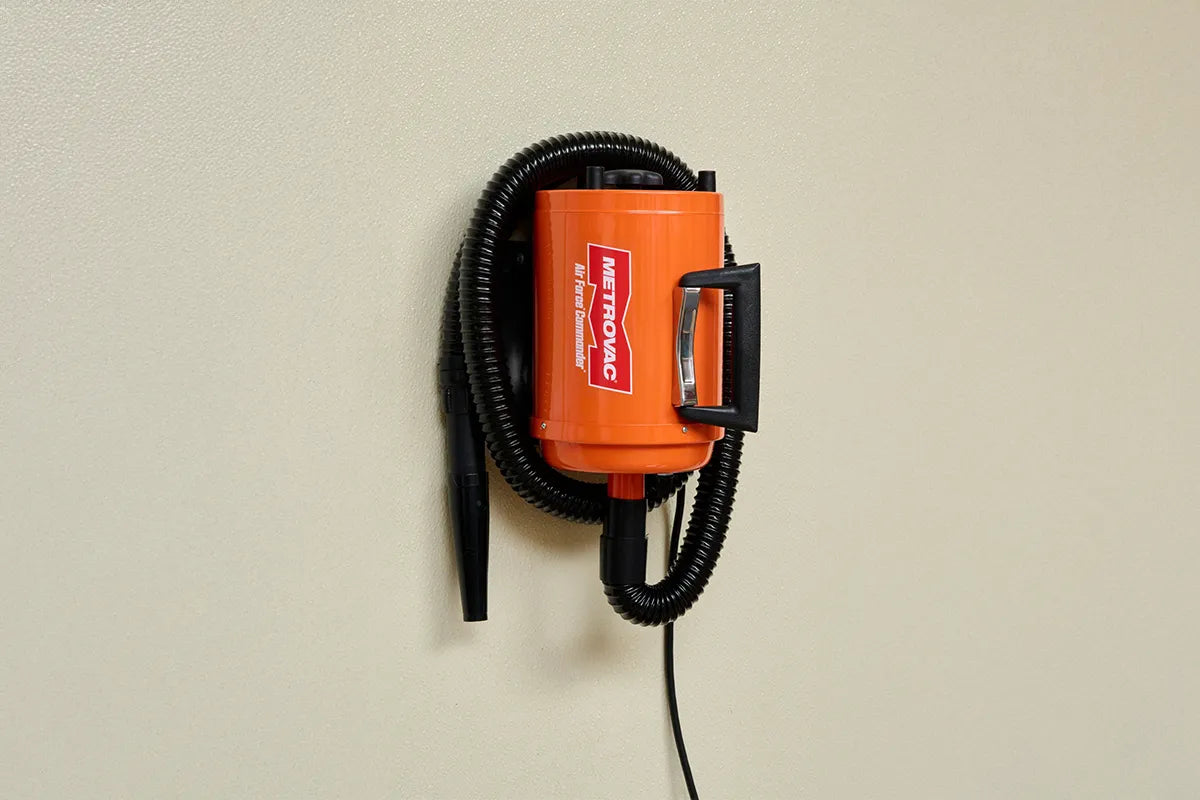 Orange MetroVac Air Force® Commander® Pet Dryer mounted on a wall with coiled hose for convenient grooming station storage.